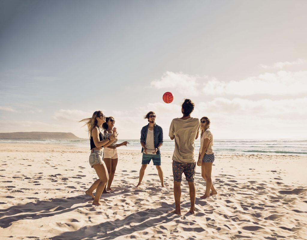 Eine Gruppe junger Leute spielt mit einem Ball am Strand. Junge Freunde genießen die Sommerferien an einem Sandstrand.